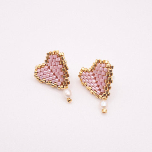 Close-up of handmade pink Miyuki beaded heart earrings with gold edging and tiny freshwater pearls, displayed on a soft white background.